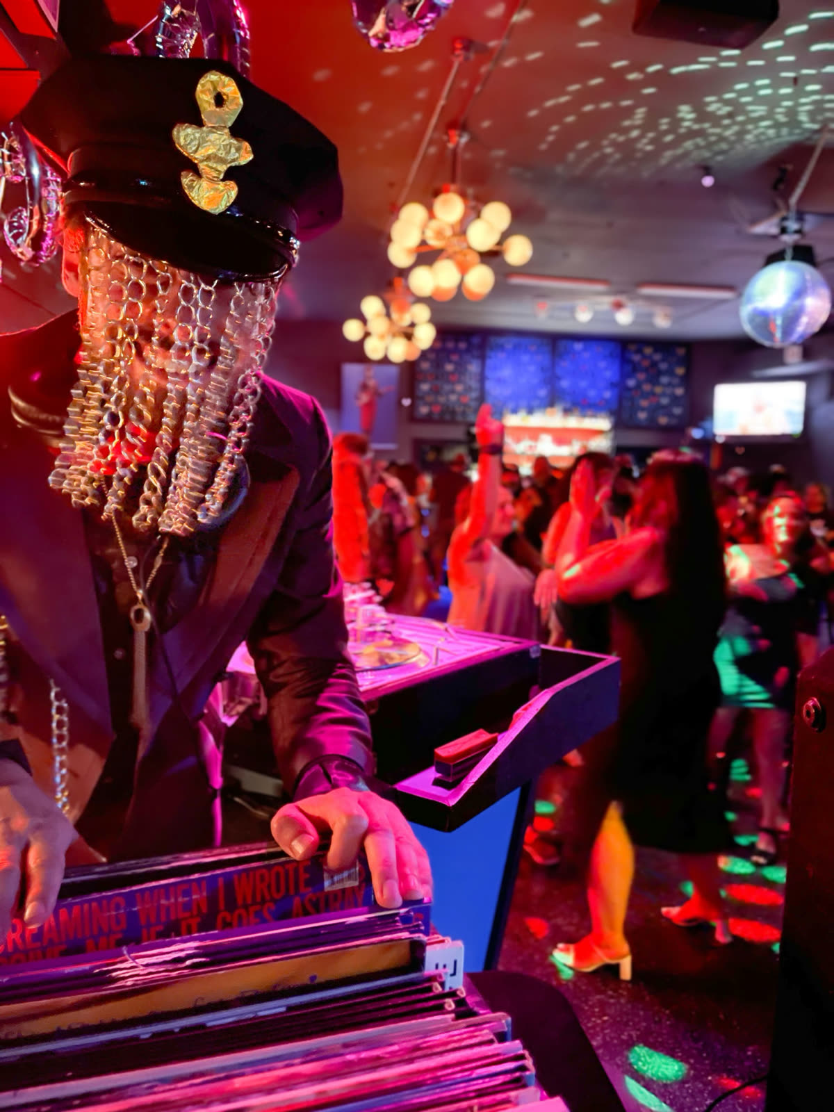 Harrison DJing a Prince birthday party from behind a crate of vinyl records, dance floor behind.